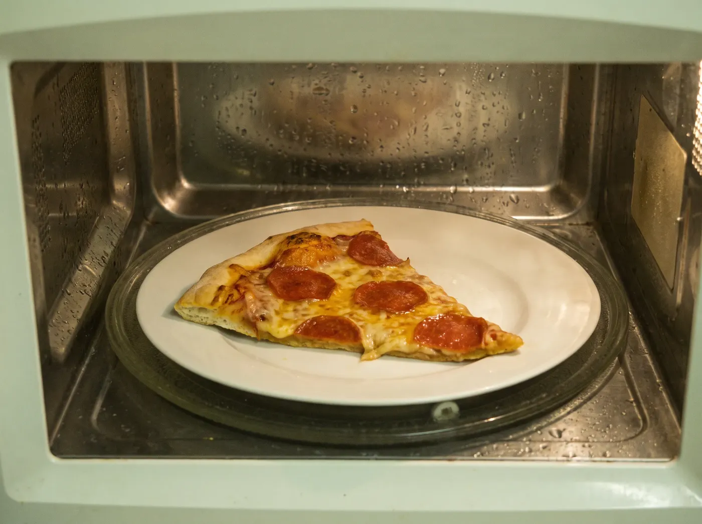 Limp reheated pizza slice on a plate inside a microwave